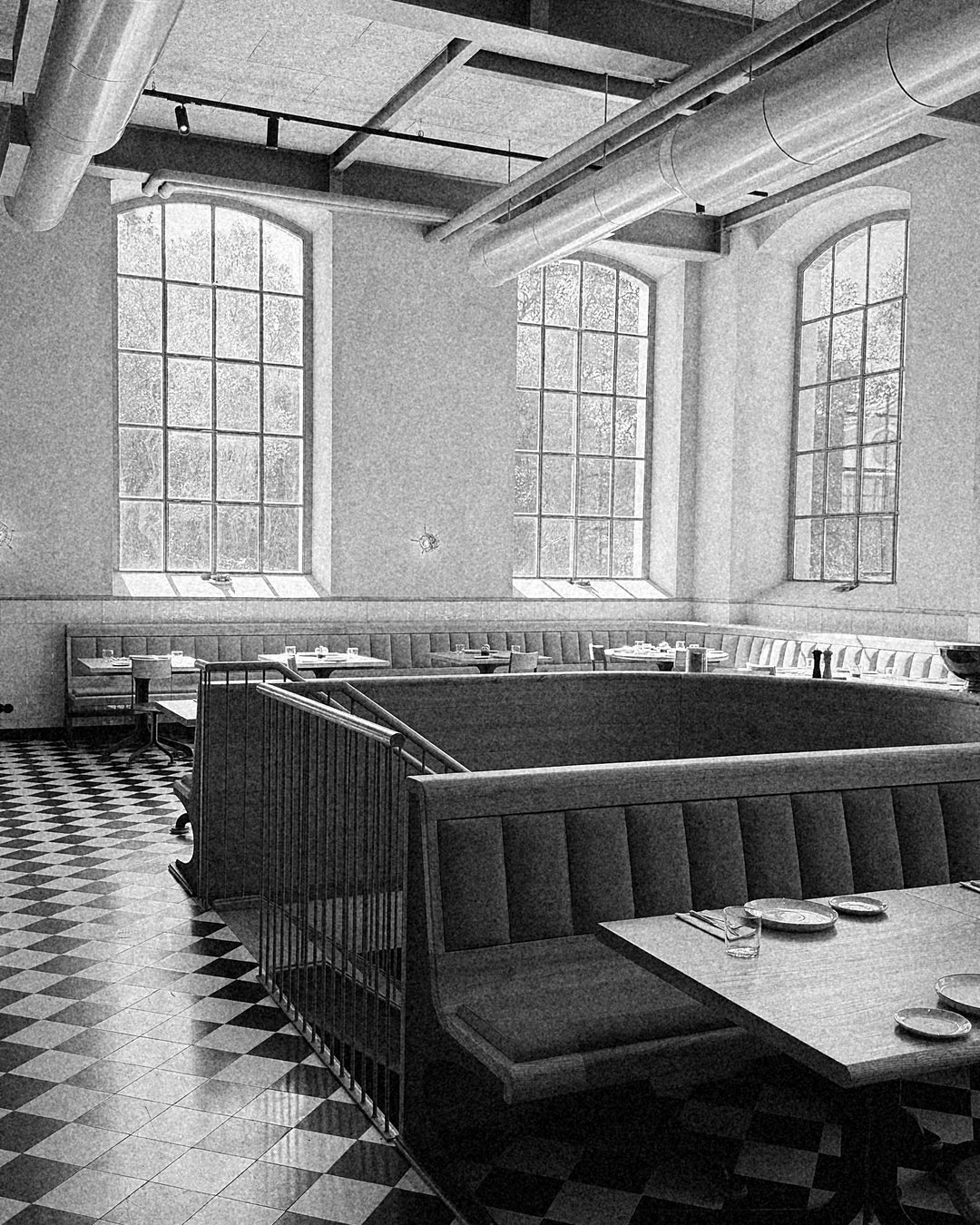 Sala com mesas de madeira, bancos verdes e chão em xadrez